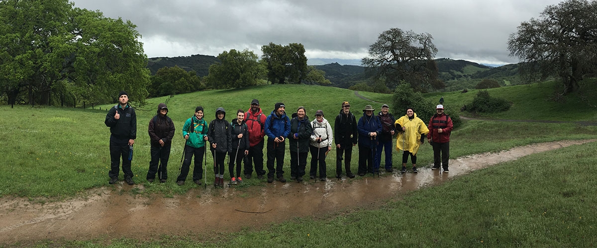 Hikers in rain jackets standing on trail facing camera and smiling