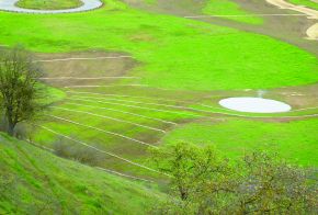 Looking down onto bright green meadow with small pond